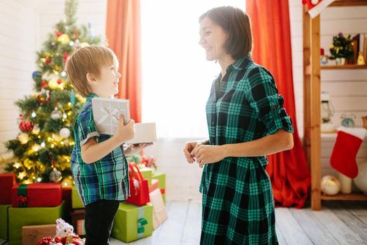 Happy family mom and son on a Christmas winter sunny morning in a decorated Christmas celebration room with a Xmas tree and gifts. .