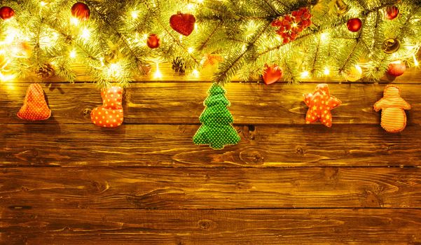 Blurred Christmas background, with fir branches, fairy lights and christmas decorations on brown wooden plank .