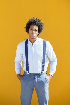 Attractive black man with afro hair on yellow urban background wearing shirt and suspenders.