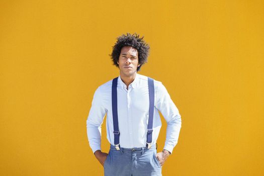 Attractive black man with afro hair on yellow urban background wearing shirt and suspenders.