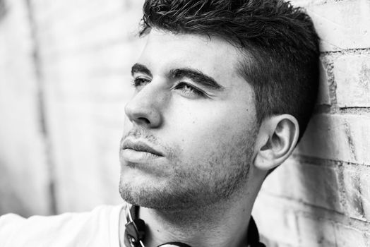 Close-up portrait of a young man with blue eyes posing near a wall. Model of fashion in urban background wearing white t-shirt