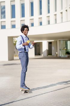 Black businessman on a skateboard holding a smartphone near an office building.