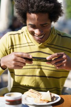 Cuban Black taking a photo with his smartphone to a snack in a bar sitting at the table outdoors on his trip to Granada, Spain.