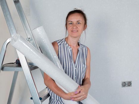 A happy woman holds rolls of new Wallpaper in her hands. Repairs in the apartment. Wallpapering.