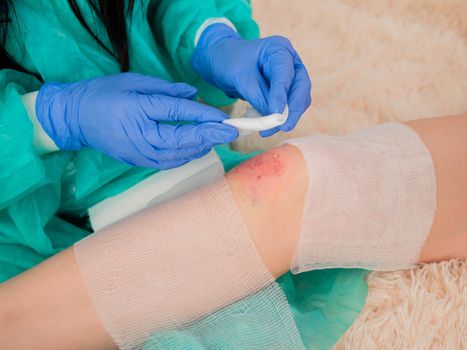 A female doctor puts a bandage on an abrasion on the knee of a teenage girl.