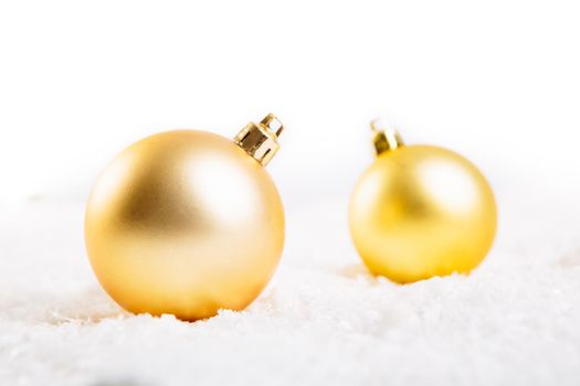 Two gold christmas balls on snow over white background .