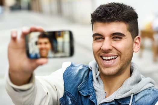 Handsome young man selfie in urban background with a smartphone wearing casual clothes