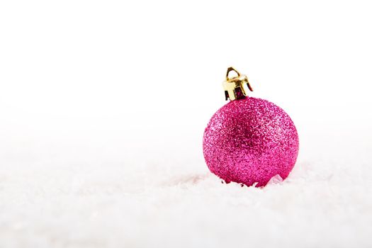 Pink christmas ball on snow over white background .