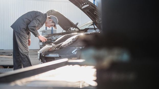 Mechanic in automobile garage checking hood for the luxury sport car, close up