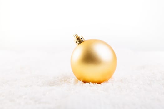 Gold christmas ball on snow over white background .