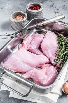 Uncooked Raw rabbit legs slices in a butcher tray with herbs. Gray background. Top view.