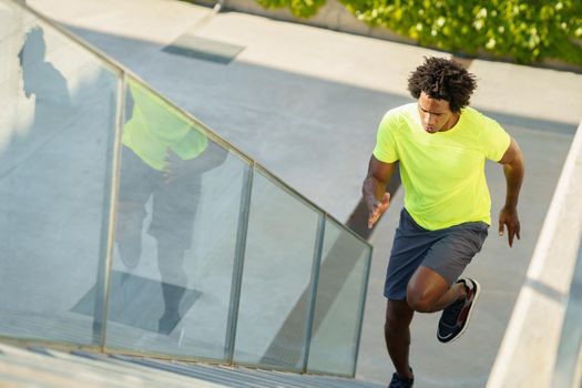 Black man running upstairs outdoors. Young male exercising in urban background.