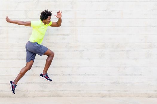 Black man training running jumps to strengthen his legs. Young male exercising in urban background.