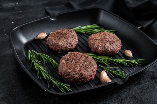 Grilled burger meat patties with spices on grill pan. Black background. Top view.