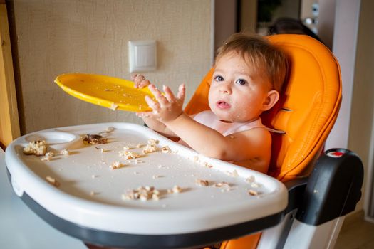 adorable baby plays with plate at the table. little child indulges in a baby chair after eating