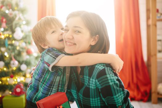 Happy family mom and son on a Christmas winter sunny morning in a decorated Christmas celebration room with a Xmas tree and gifts. .