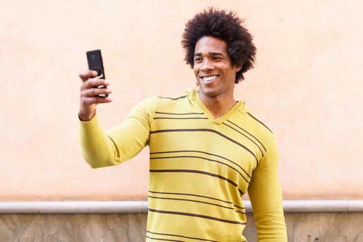 Black man with afro hair and headphones using smartphone taking photographs