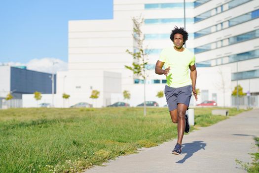 Black athletic man, afro hairstyle, running in an urban park. Young male exercising in urban background.