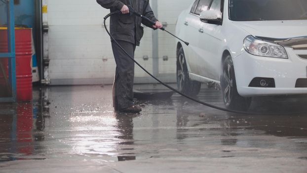 Worker in auto service is washing a car in the suds by water hoses, telephoto