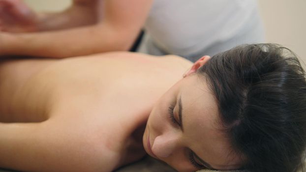 Young pretty half-nude female relaxing in spa salon - oil sesame massage table, close up