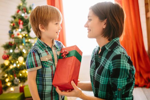 Happy family mom and son on a Christmas winter sunny morning in a decorated Christmas celebration room with a Xmas tree and gifts. .