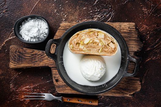 Apfelstrudel strudel with cinnamon, powdered sugar and vanilla ice cream in a pan. Dark background. Top view.