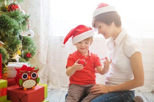 Mother with her Little son decorating christmas tree at home. Family preparing home for xmas celebration.