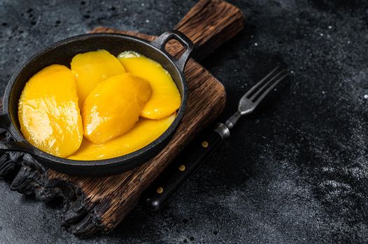 Canned mango slices in bowl. Black background. Top view. Copy space.