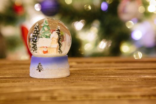 Christmas snow globe on wooden table over christmas lights .