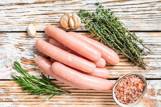 Raw Chicken sausages on a wooden kitchen table with herbs. White wooden background. Top view.