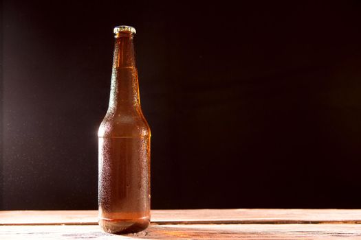 Bottle of beer on wooden table on a black background