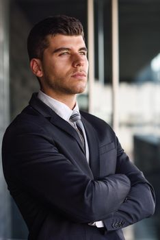 Young businessman near a modern office building wearing black suit and tie. Man with blue eyes