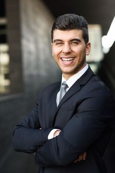 Young businessman near a modern office building wearing black suit and tie. Man with blue eyes smiling.