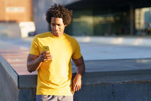 Black man with afro hair consulting his smartphone with some exercise app while resting from his workout.