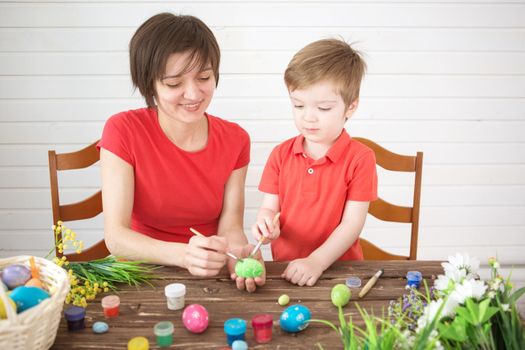 Easter preparations. Happy young mother spending time with her joyful son. Happy family Mom and children son paint easter eggs with colors. Preparation for Easter holiday.