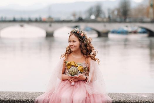 a little girl in a pink Princess dress with a bouquet in her hands walks through the old city of Zurich.Portrait of a girl in a pink dress on a city street in Switzerland.