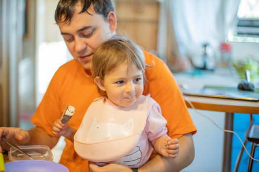 adorable caucasian toddler sitting with father at the table. dad feeding baby, single parent with little child