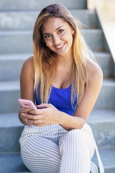 Young female using smartphone wearing casual clothes. Girl sitting outdoors.