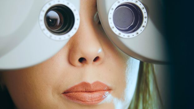 Ophthalmology concept - young woman checks the eyes on the modern equipment in the medical center, close up