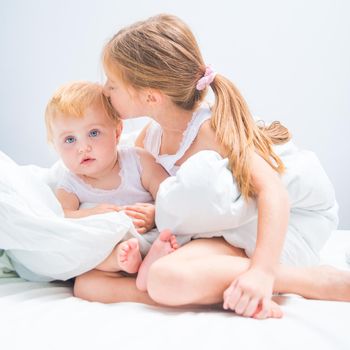 Two sweet little sisters in white T-shirts in bed