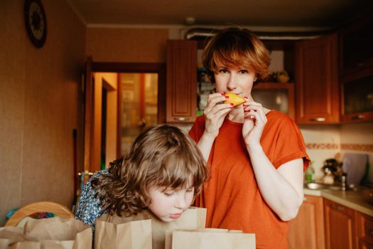 Woman and little girl standing together in kitchen with groceries in paper bags