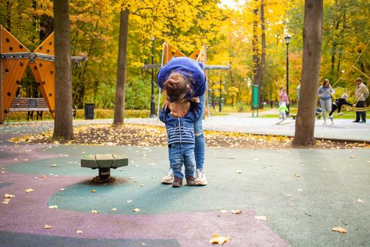Mom and toddler in blue clothes play fun on the playground in the autumn park. happy childhood concept.
