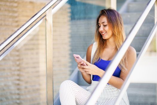 Young woman using a touchscreen smartphone wearing casual clothes. Girl sitting outdoors with gel nails.