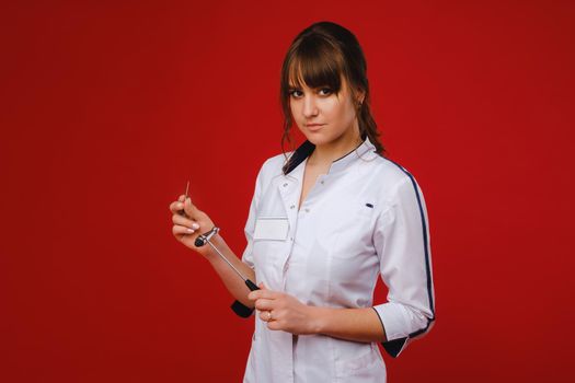 a beautiful doctor girl holds a reflex hammer and smiles at the camera isolated on a Red background.