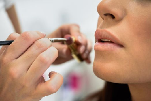 Makeup artist making up lips of an African young woman in a beauty center.. Beauty and Aesthetic concepts.