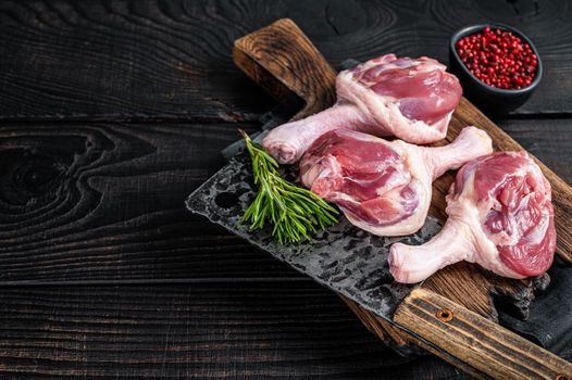 Raw Duck thighs on butcher board with meat cleaver. Black wooden background. Top view. Copy space.