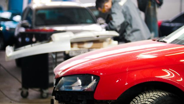 Defocused background - professional car service - man work tinsmith works with a hammer - repairing automobile, telephoto