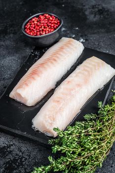Raw cod loin fillet fish on marble board. Black background. Top view.