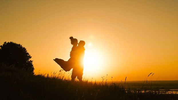 Young loving couple - brave young man and beautiful girl at sunset silhouette, dancing telephoto shot