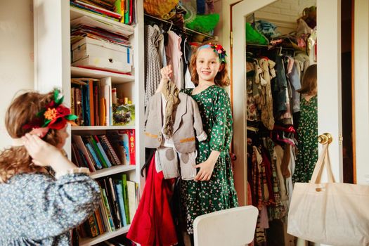 Cheerful girl standing with various garments for festive events near wardrobe and looking at camera